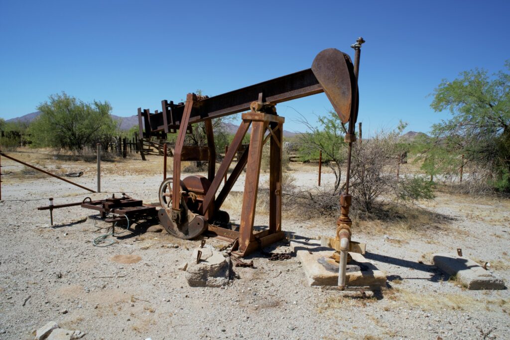 Abandoned rusty oil pumpjack in a barren desert landscape under clear blue skies.