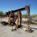 Abandoned rusty oil pumpjack in a barren desert landscape under clear blue skies.