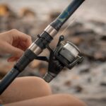 A person handling a fishing rod and reel by a rocky riverside, enjoying a peaceful outdoor hobby.