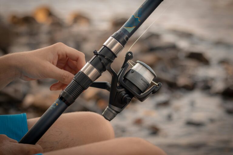 A person handling a fishing rod and reel by a rocky riverside, enjoying a peaceful outdoor hobby.